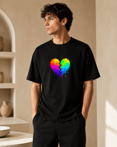 Man wearing a black t-shirt with a colorful heart design in a room with shelves.